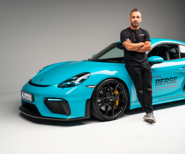 Serdar Berse lehnt sich an einen blauen Porsche